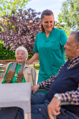 two residents outside sitting down with a care working smiling with them