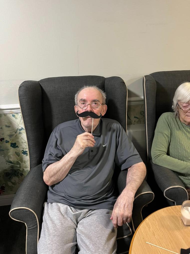 older man sat down holding up a fake moustache